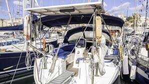 Eine Segelyacht liegt in einer Marina festgemacht, mit einer überdachten Deckfläche, sichtbarer Ausrüstung und einem Rettungsring.