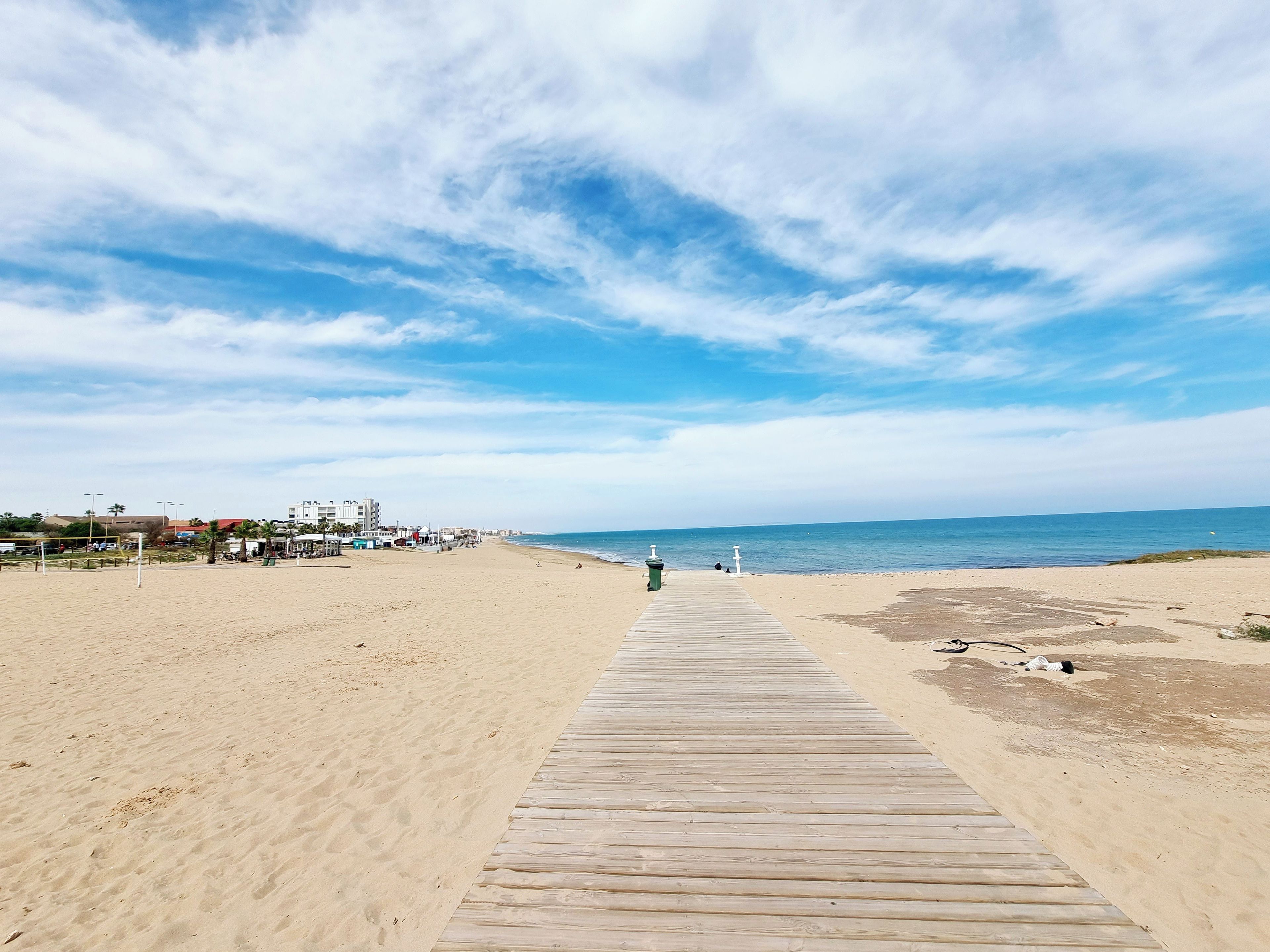 A wooden boardwalk leading to a beach with a clear sky.