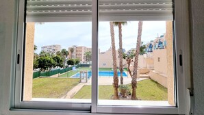 Blick durch ein Fenster mit einer Schiebetür, der einen Pool, Palmen und Gebäude im Hintergrund zeigt.