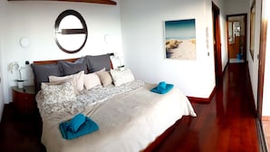 Camera da letto con un letto grande, un comodino, uno specchio, una sveglia a muro e un quadro a tema spiaggia.