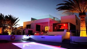 Un edificio moderno con tetto piatto, ampie finestre e area piscina con pavimento illuminato.