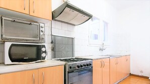 A kitchen with a double microwave, a stove, and wooden cabinets. - Room in Guest Room - Private Room With 200m2 Sunny Terrace 6 (Barcelona)