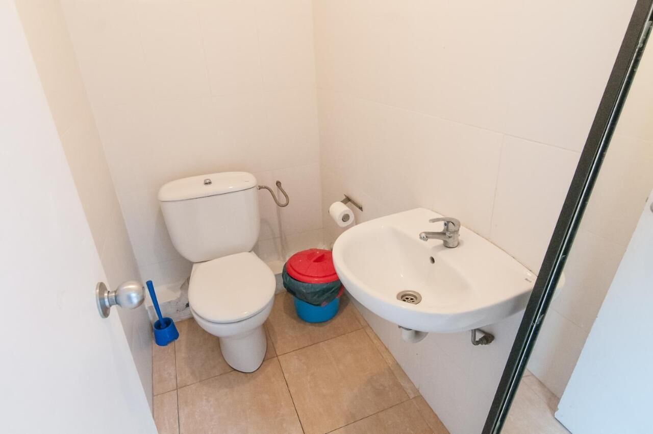 A small bathroom with a toilet, a sink, and a blue and red trash bin.