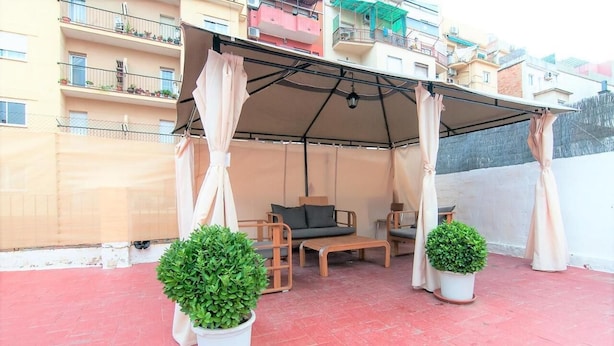 A covered outdoor seating area with two sofas and a table, surrounded by potted plants. - Room in Guest Room - Private Room With 200m2 Sunny Terrace 6 (Barcelona)