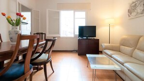 A living room with a television, a sofa, a dining table with chairs, and a vase of flowers. - Room in Guest Room - Private Room With 200m2 Sunny Terrace 6 (Barcelona)