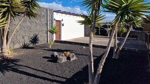 A courtyard with palm trees, a stone wall, and a white building with a red door. - Villa Georgiana Spacious Quiet 4 Bed Property With Private Pool Sleeps 8 (Yaiza)