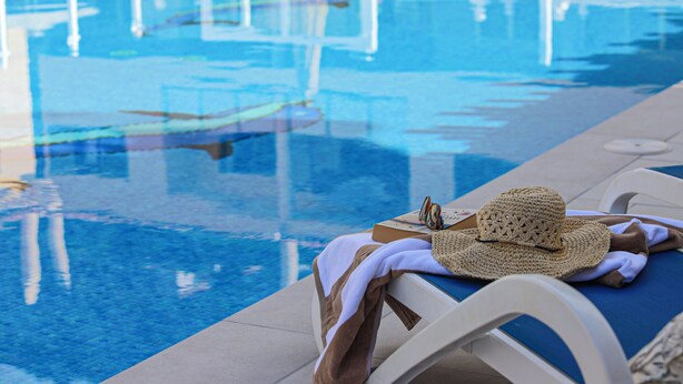 Un espace aménagé au bord de la piscine, avec une chaise longue, un chapeau en fibres naturelles et un livre.