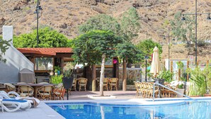 Area piscina con lettini, una zona relax coperta e montagne sullo sfondo.