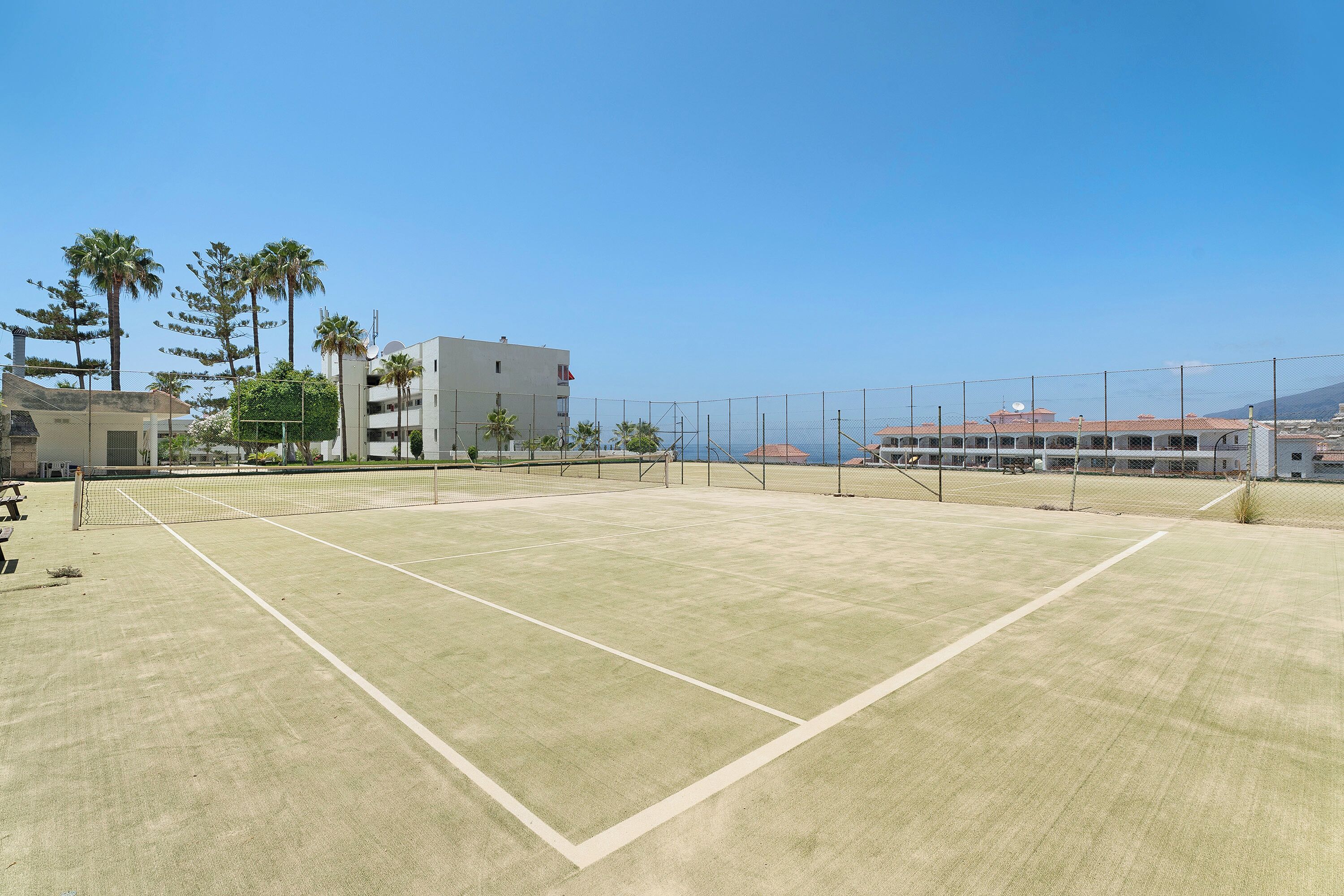 A tennis court with a net, surrounded by buildings and palm trees.