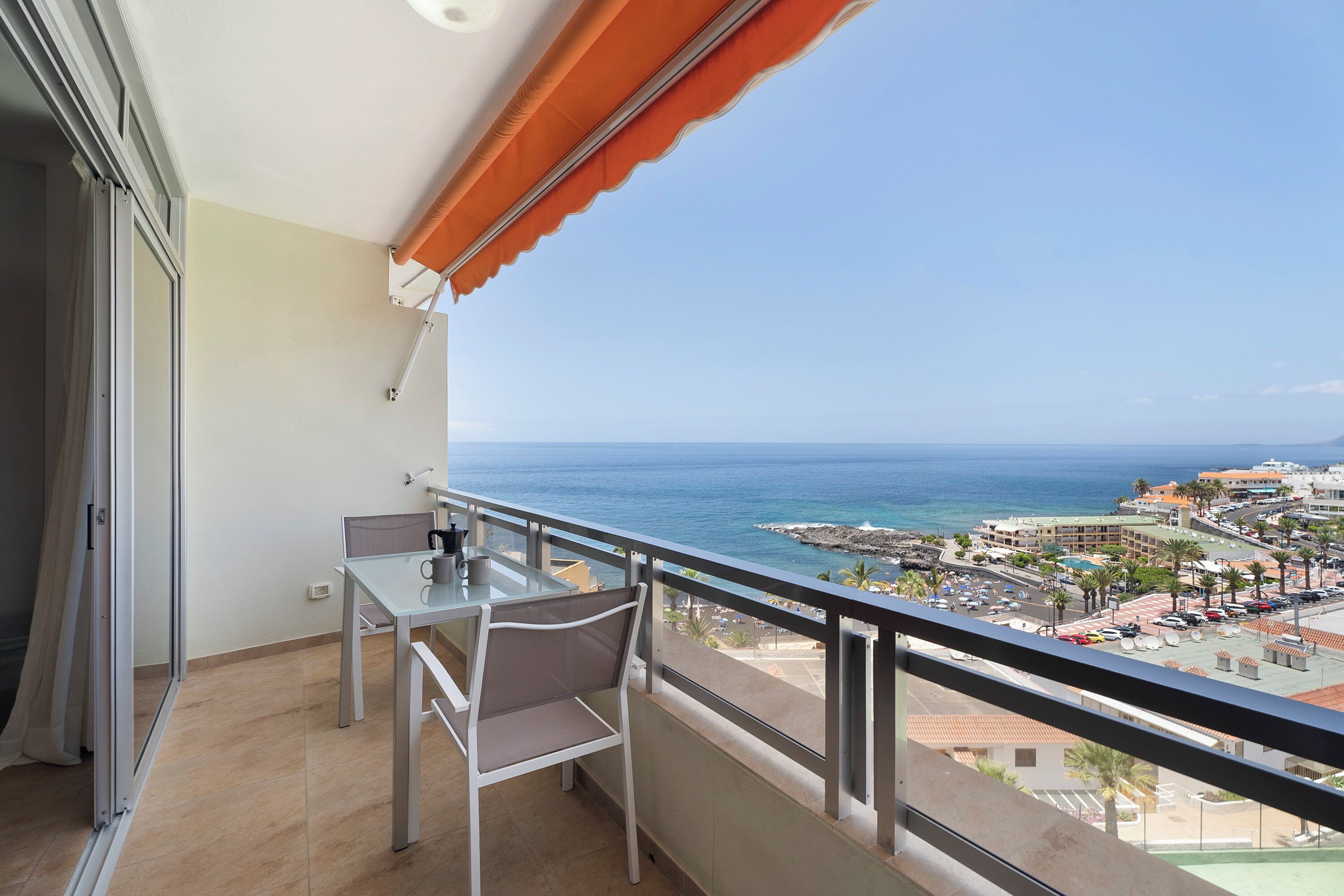 Un balcón con mesa y silla, con vista a un pueblo costero y al mar.