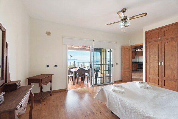 A bedroom with a bed, wooden furniture, a ceiling fan, and a sliding glass door leading to an outdoor area with a table and chairs. - Rural House Tijoco Bajo & With Jacuzzi Adeje (Adeje)