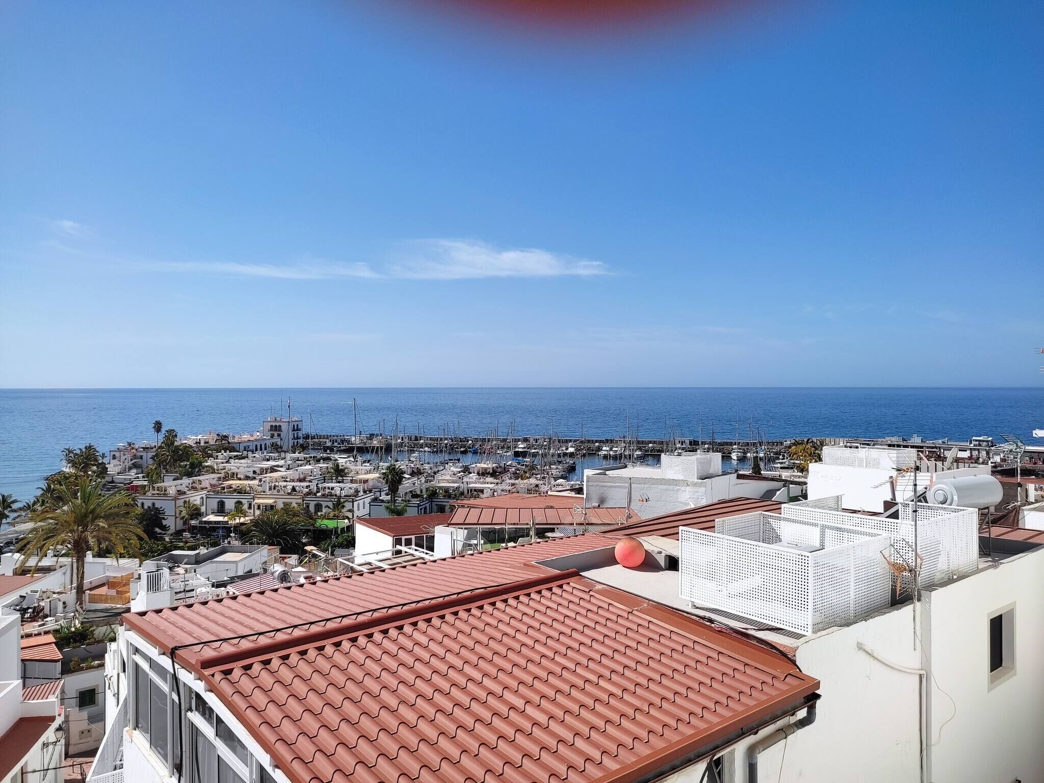 A coastal town with white buildings, red-tiled roofs, and a marina with boats.