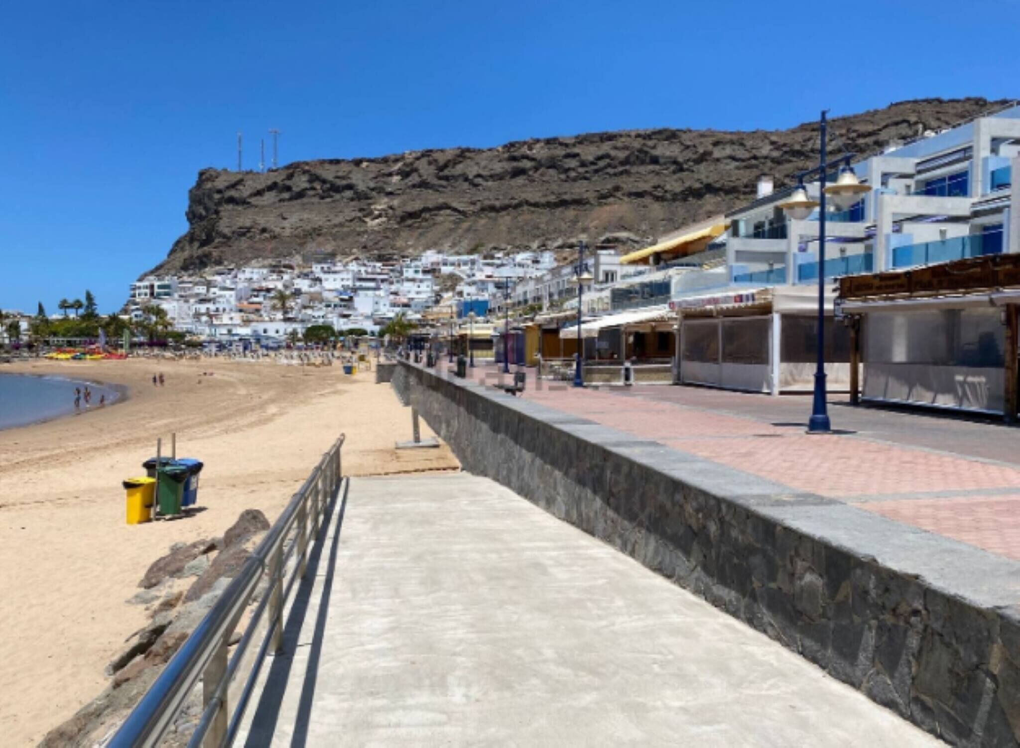 Une promenade en bord de mer, avec un mur de pierre, une plage et des bâtiments en arrière-plan.