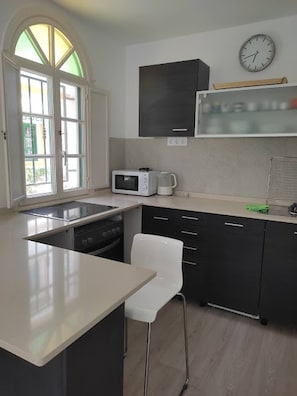 Una cocina compacta con microondas, un lavamanos y una silla.