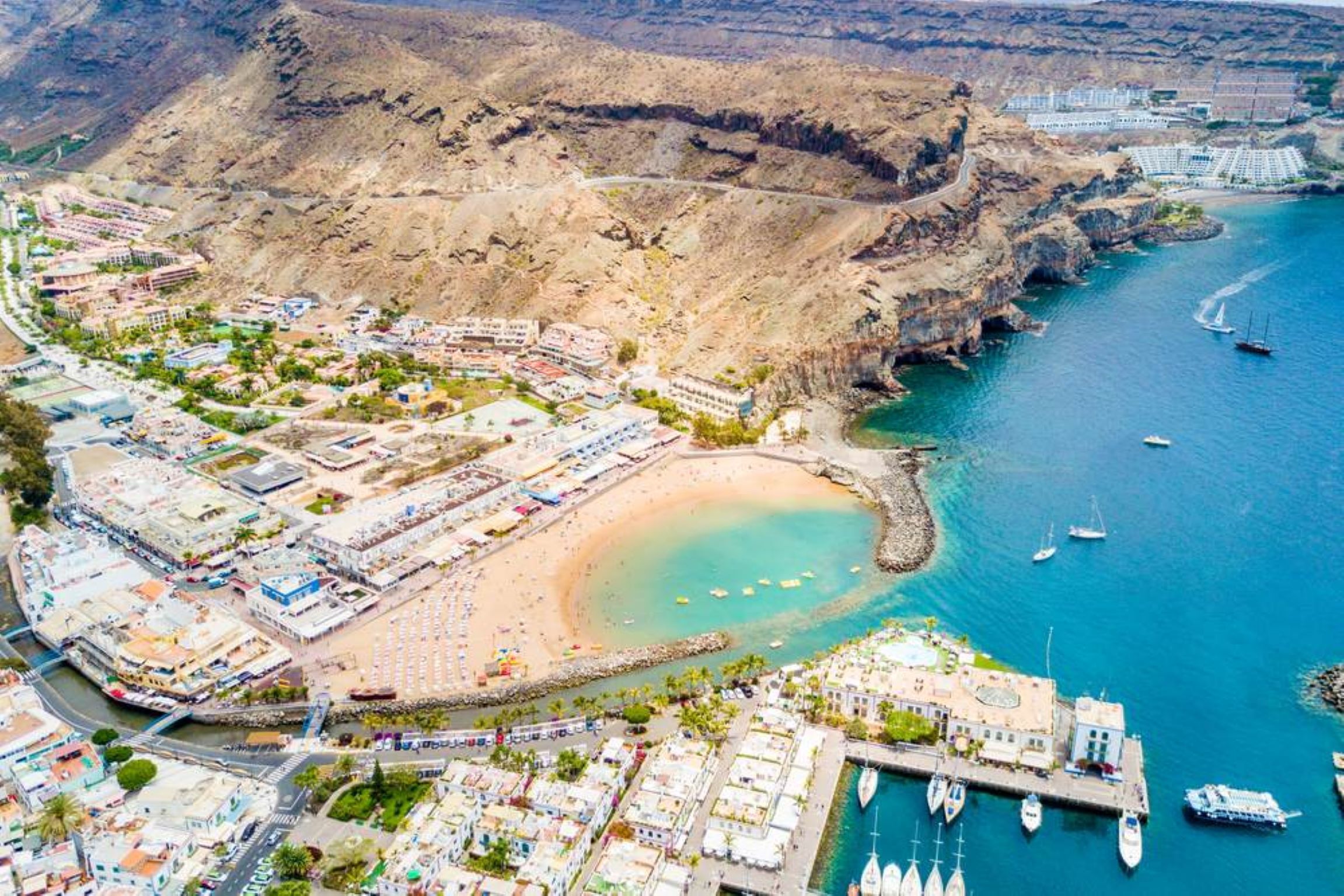 Vista aérea de un pueblo costero con playa, puerto deportivo y edificios.