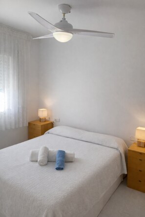 A bedroom with a bed, two bedside tables, a ceiling fan, and a window with curtains. - Beautiful And Bright Apartment In Calafell, (El Vendrell)