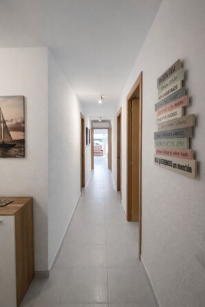 A hallway with a wooden desk, a framed picture on the wall, and a sign with text. - Beautiful And Bright Apartment In Calafell, (El Vendrell)