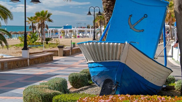 A blue and white boat sculpture with an anchor, located on a paved walkway with palm trees and a beach in the background. - Playamar, Torremolinos, Beautiful Apartment by the Sea (Torremolinos)