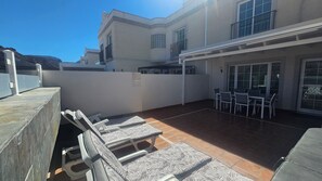 A patio with outdoor furniture, a covered seating area, and a building with a tiled roof. - Luxury Renovated Duplex With Pools & Private Jacuzzi! (Mogan)
