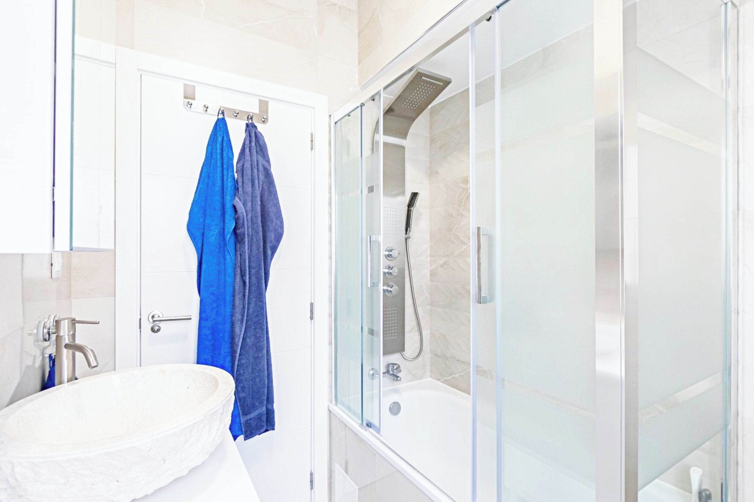 Un bany modern amb una dutxa envidrada amb vidre, un lavabo blanc i una tovallola blava penjada a la porta.