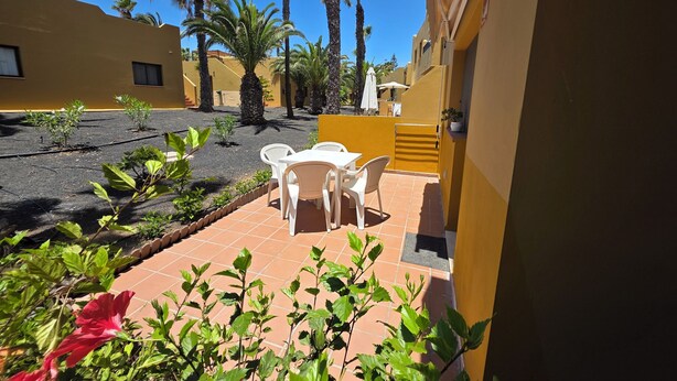 A courtyard with a table and chairs, surrounded by plants and palm trees. - Casa Manba, Terrace, Pool and Wifi (La Oliva)