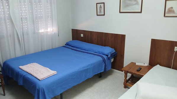 Una habitación de hotel con una cama individual, una mesita de noche con un control remoto y una silla blanca.