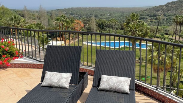 Two lounge chairs with pillows on a balcony overlooking a pool and a scenic landscape. - Spectacular Penthouse Apartment in Magnificent San Roque Club (San Roque)