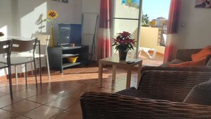 Ein Wohnzimmer mit einer Couch, einem Esstisch mit Stühlen, einem Fernseher und einer Topfpflanze.