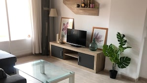 Ein modernes Wohnzimmer mit einem Glastisch, einer Couch, einem Fernseher auf einem Holzboden und einer Topfpflanze.