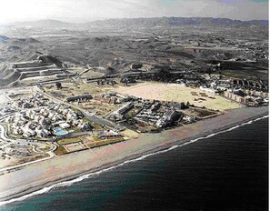 Vue aérienne d’une station balnéaire comprenant plusieurs bâtiments, une plage et un port de plaisance.