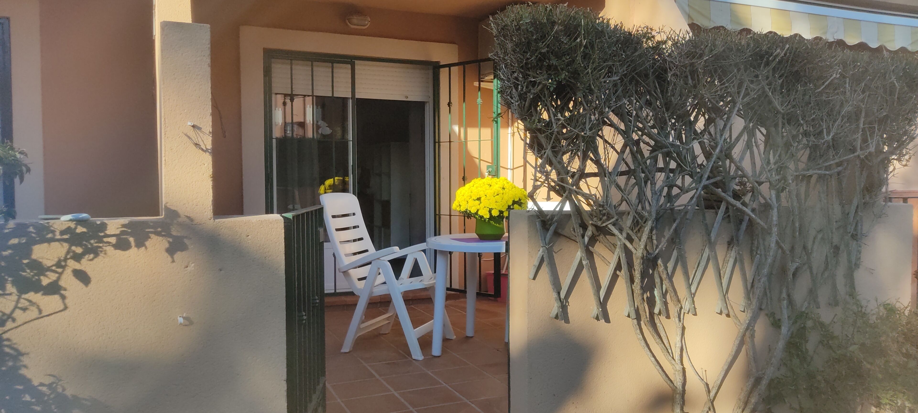 A balcony with a white chair and a small table, a potted plant, and a yellow flower arrangement.