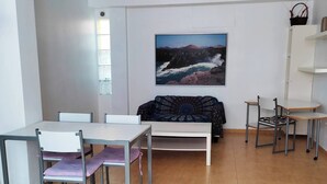 Un salon moderne comprenant un coin repas, un canapé et un tableau représentant un paysage côtier.