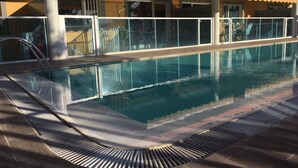 Une piscine dotée d’une paroi en verre, d’une rambarde métallique et d’une terrasse carrelée.