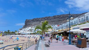 Une promenade en bord de mer, avec une falaise rocheuse en arrière-plan, des boutiques et un espace café.