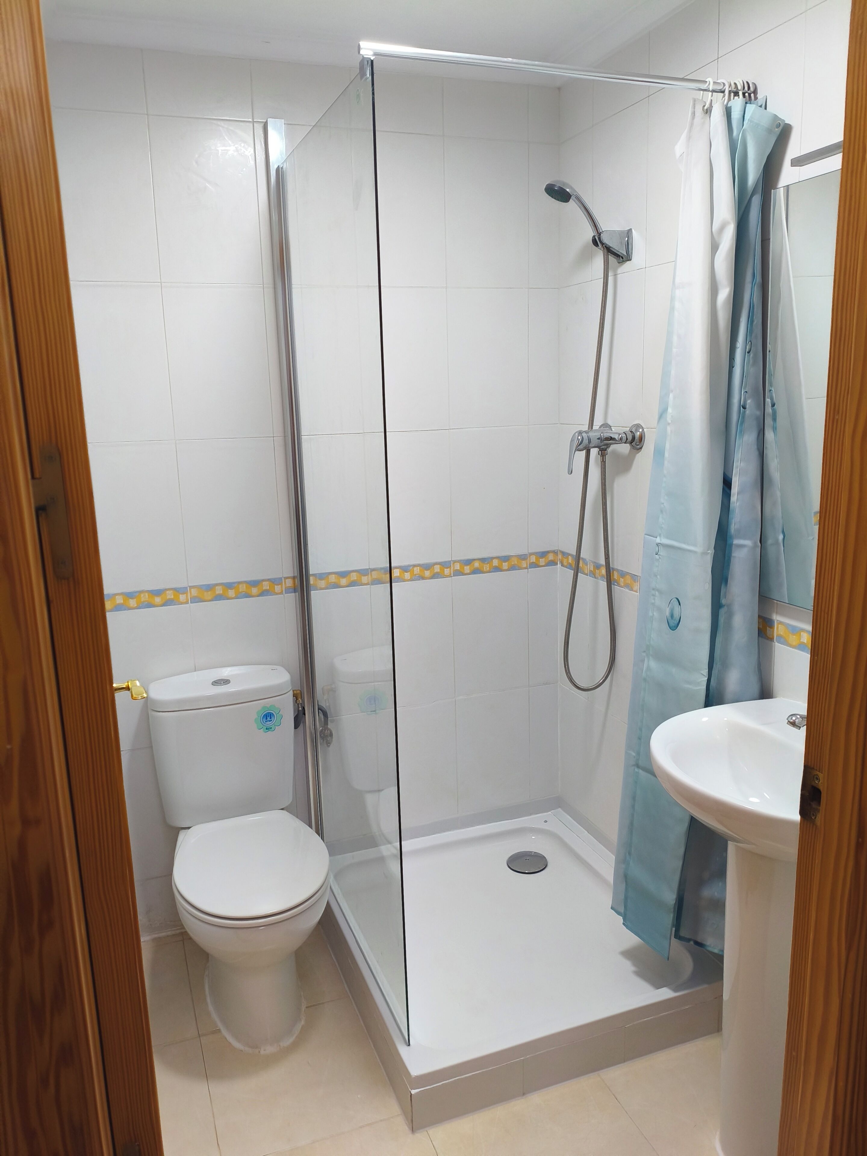 Een badkamer met een douchecabine van glas, een wit toilet en een wastafel op een voetstuk.