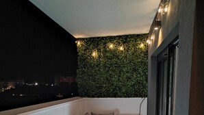Un balcón con césped artificial verde, un conjunto de sofás de mimbre y una guirnalda de luces.