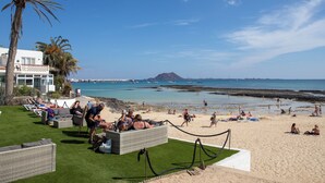 A beachside area with lounge chairs and a pool, overlooking the sea and a mountain in the distance. - Casa Frida With High-speed Wifi and Smart-tv (La Oliva)