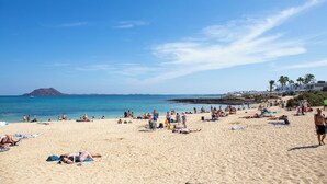 A beach with people sunbathing and swimming, a clear sky, and a distant mountain. - Casa Frida With High-speed Wifi and Smart-tv (La Oliva)