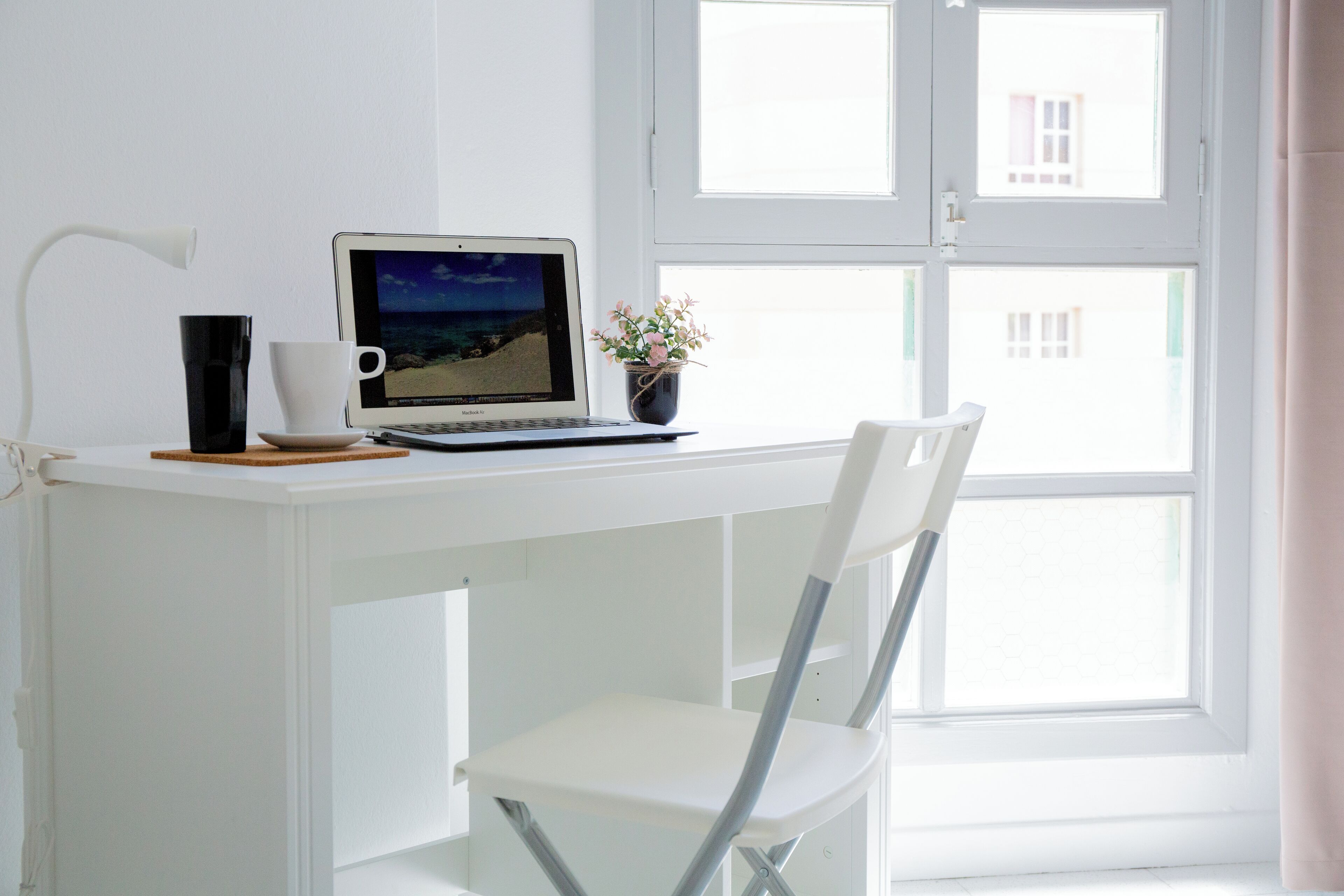 A white desk with a laptop, a cup, and a small plant.