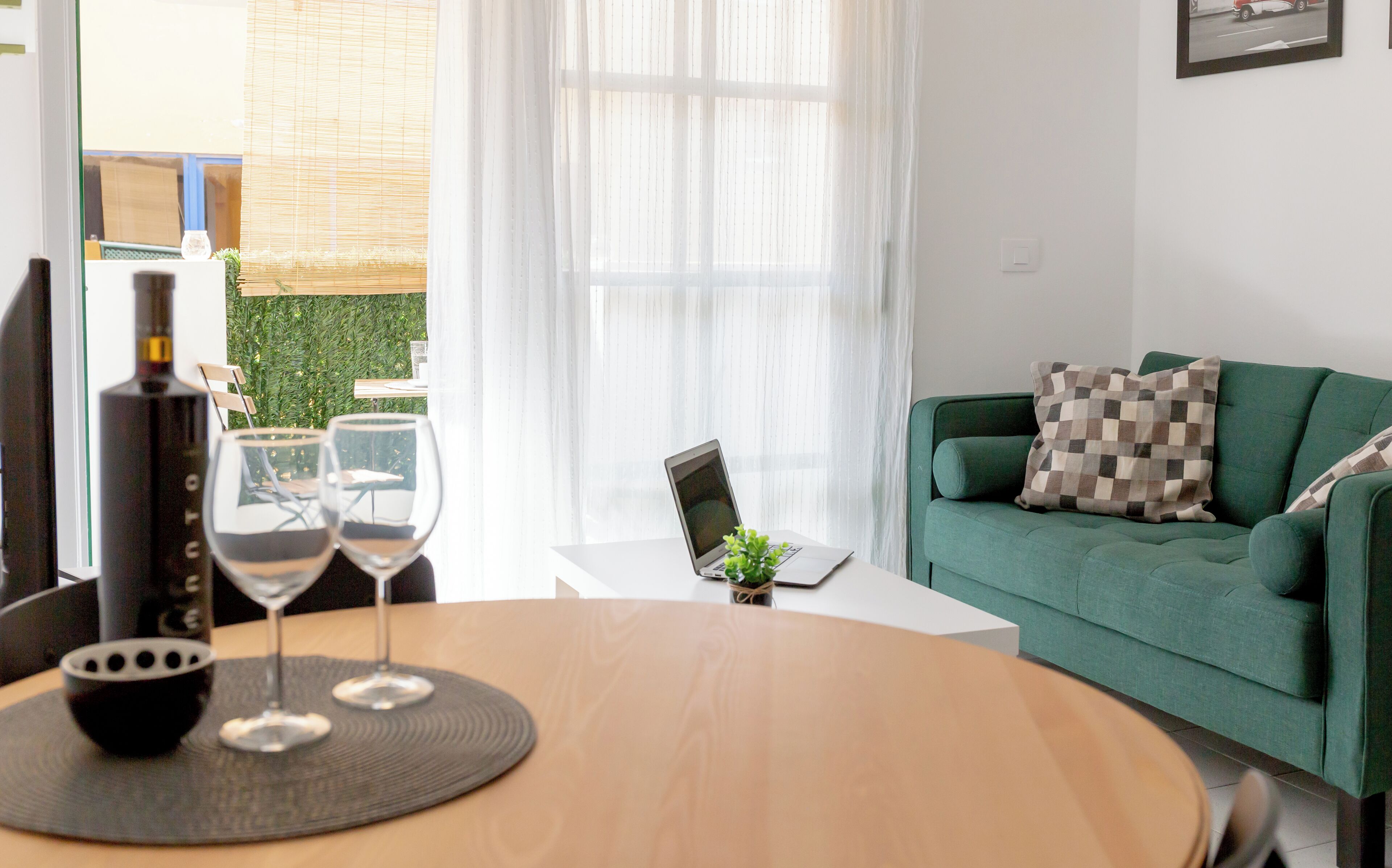 Ein modernes Wohnzimmer mit einem grünen Sofa, einem Laptop auf einem kleinen Tisch und zwei Weingläsern auf einem runden Tisch.