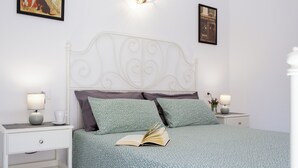 A neatly made bed with a patterned bedspread, two pillows, and an open book on the bed. There are two bedside tables with lamps and a small plant on one. - Casa Frida With High-speed Wifi and Smart-tv (La Oliva)