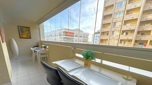 Un balcone con una scrivania bianca, due sedie, un vaso con una pianta e vista sulla città.