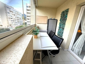 A balcony with a white table, black chairs, a potted plant, a grey cabinet, and a decorative wall panel.
