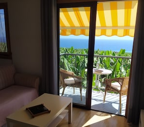 Une pièce comprenant un canapé, une table et un balcon avec des fauteuils et une table en osier.