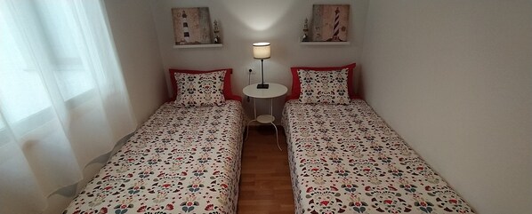 Una habitación con dos camas individuales, una mesita con lámpara y obras de arte en las paredes.
