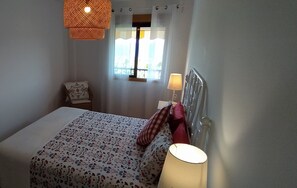 A bedroom with a bed, a bedside lamp, a window with curtains, and a hanging light fixture. - Caracol "trail Mountain La Palma" - Junto a Trébol (Tazacorte)