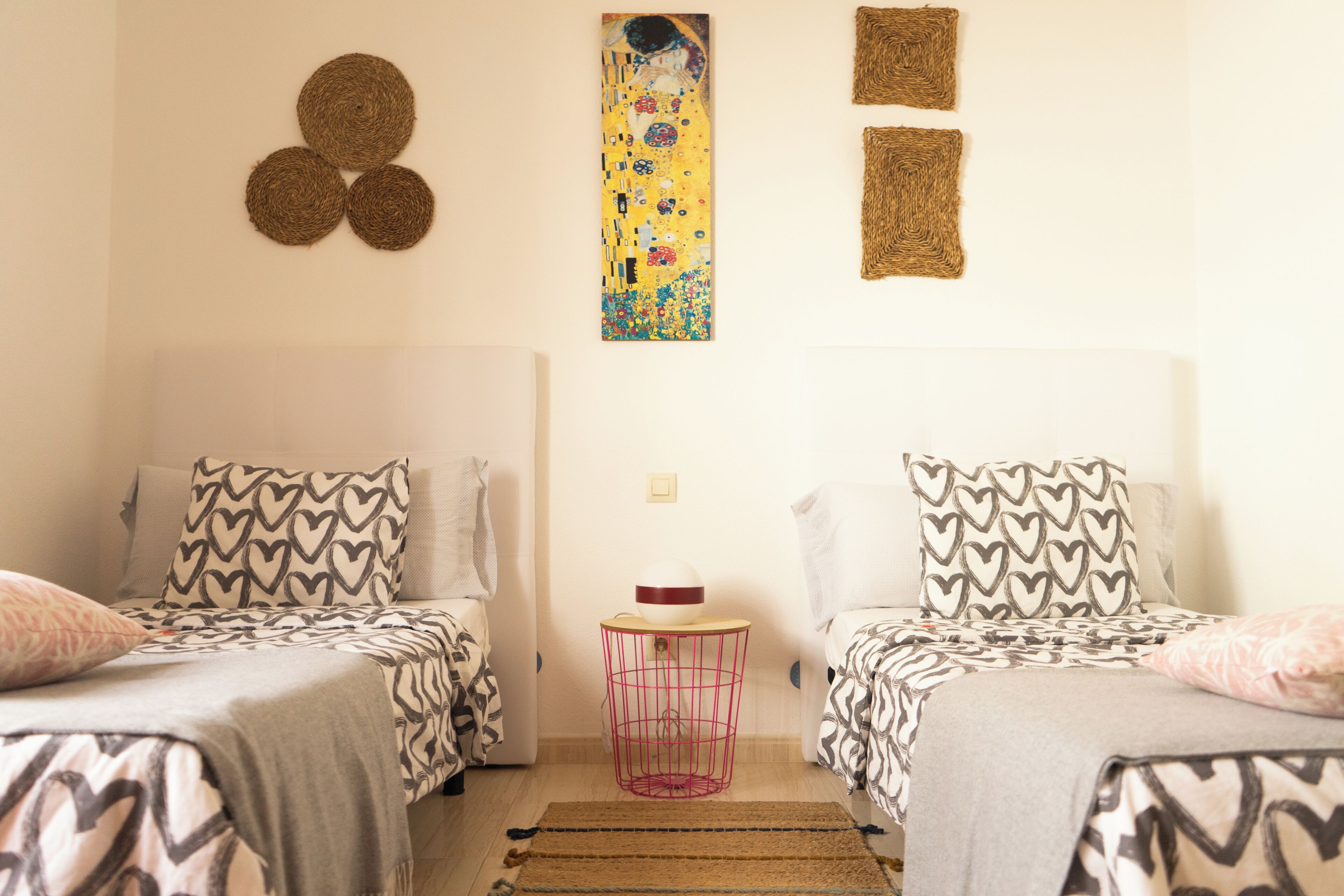A bedroom with two beds, patterned bedding, a small round table, and wall art.