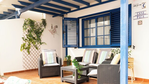 A cozy patio area with wicker furniture, a tiled floor, and a blue window frame. - Casa Paca - Your Private Oasis in Lanzarote - Paradise by the Sea (Yaiza)