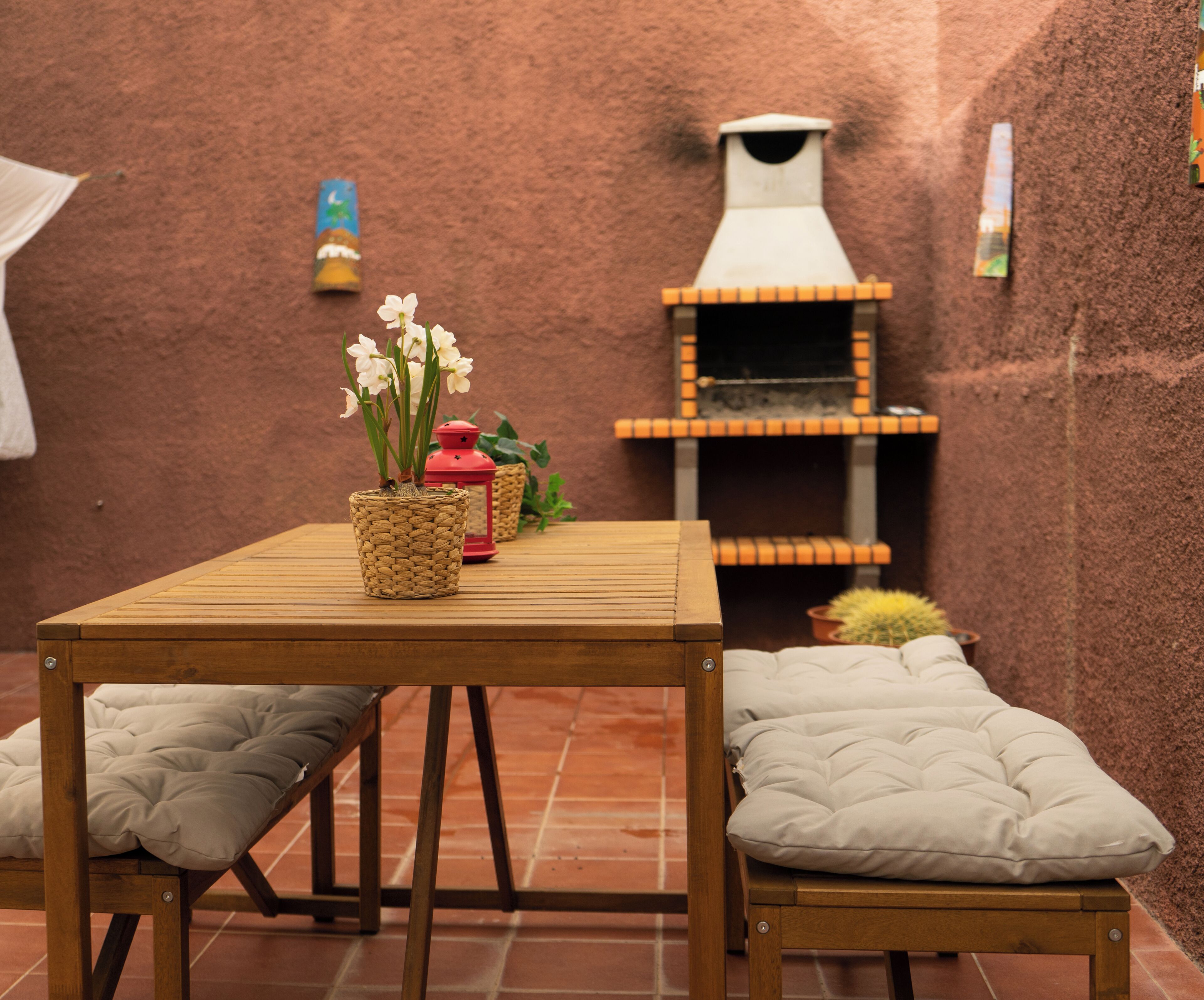 A wooden table with two cushioned chairs, a red lantern, and a small potted plant with white flowers.