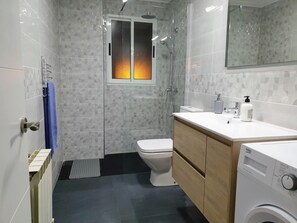 A modern bathroom with a shower, toilet, and washing machine. - Aviles vut 1963 as jj (Aviles)